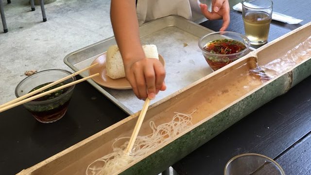 流しそうめんを箸ですくう子供